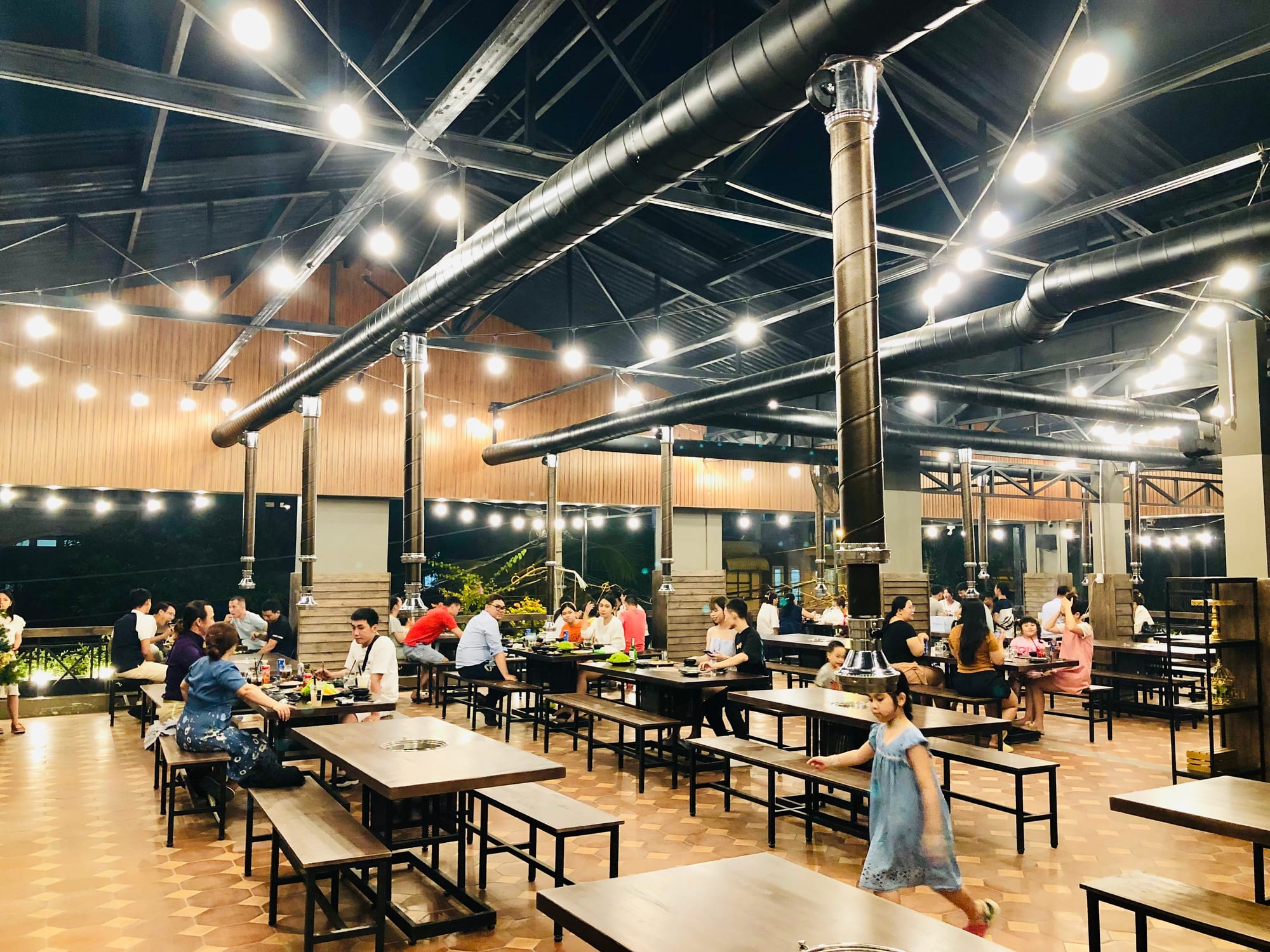 A lively communal dining area with bright LED lighting and guests seated at long tables on an evening out