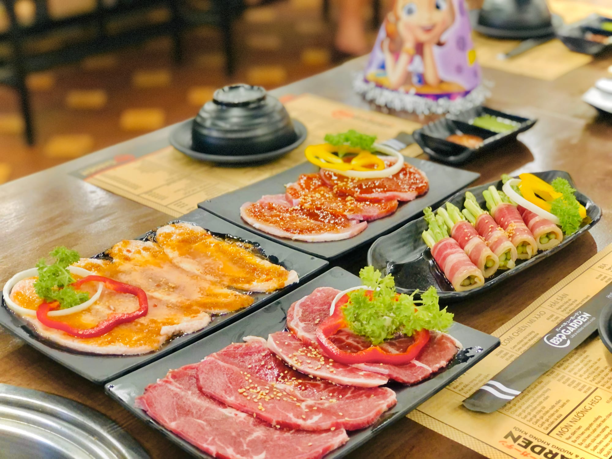 Assorted raw meats including beef, chicken, and pork served on black plates ready for the grill
