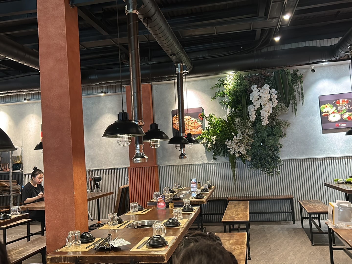 Industrial-style restaurant interior with pendant lighting, wood tables, and white flowering vines on the accent wall